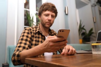 Photo of Handsome man using smartphone at table in cafe, focus on hand