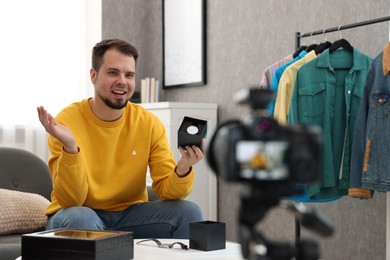 Photo of Smiling fashion blogger showing wristwatch while recording video at home