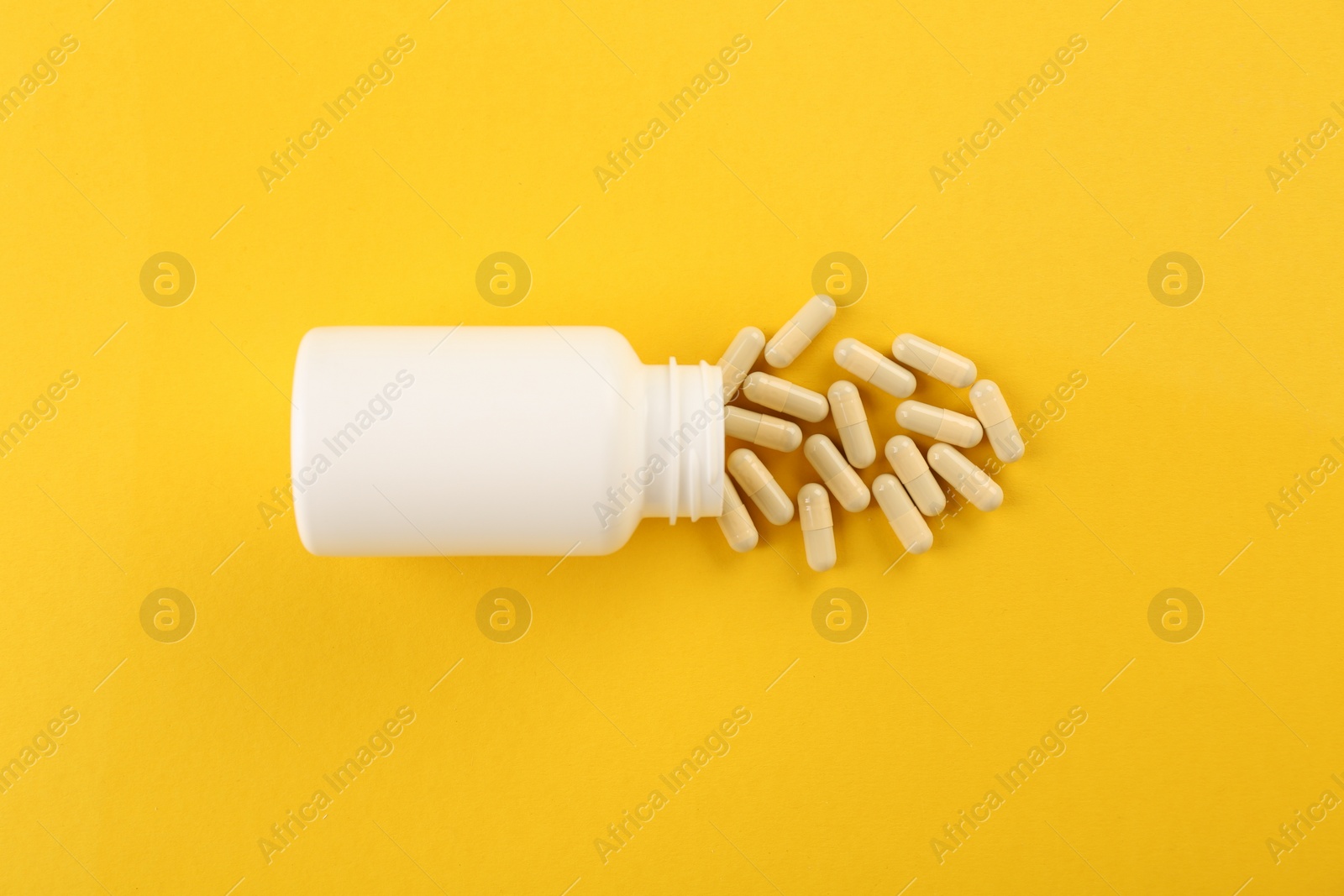 Photo of Bottle and vitamin capsules on yellow background, top view