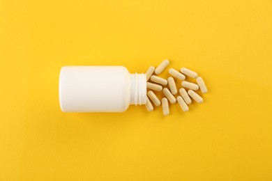 Photo of Bottle and vitamin capsules on yellow background, top view