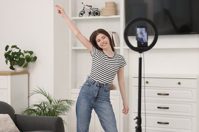 Photo of Smiling teenage blogger dancing while streaming at home