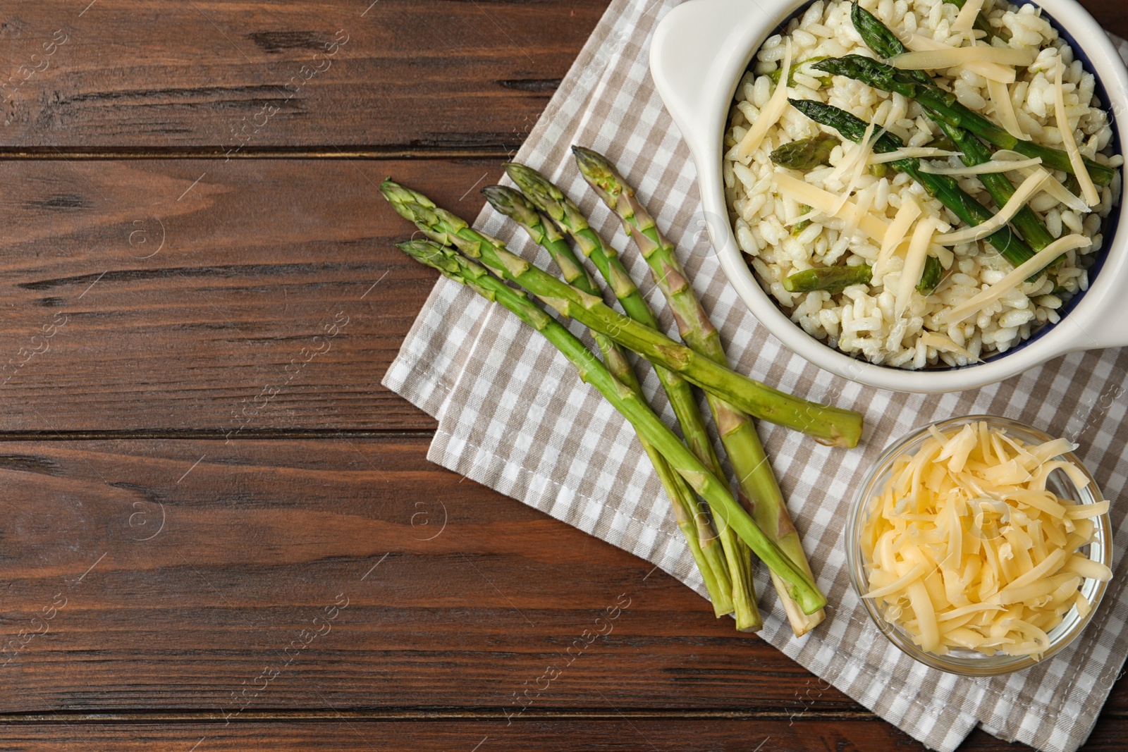 Photo of Delicious risotto with asparagus served on wooden table, flat lay. Space for text