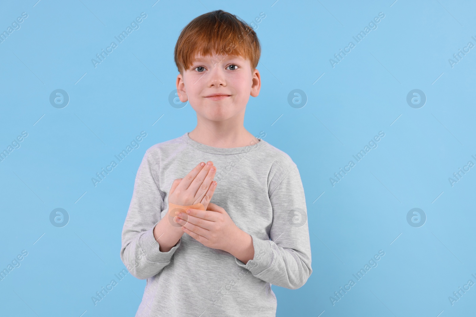 Photo of Little boy putting sticking plaster onto hand on light blue background