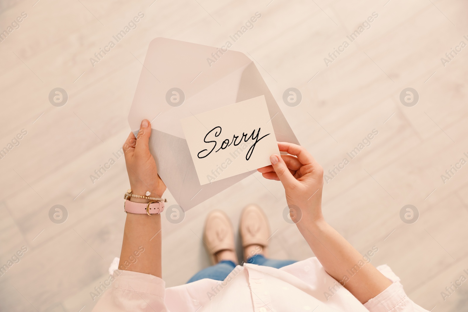 Image of Woman receiving apology message indoors, top view. Card with word Sorry