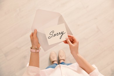 Image of Woman receiving apology message indoors, top view. Card with word Sorry