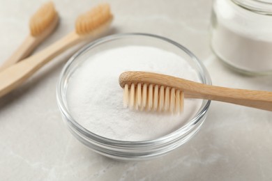 Photo of Bamboo toothbrush and glass bowl of baking soda on light table, closeup