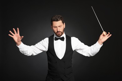 Professional conductor with baton on black background