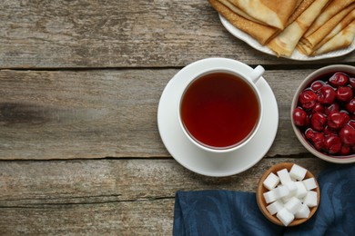 Photo of Cup of tea, cherry and crepes on wooden table, flat lay. Space for text