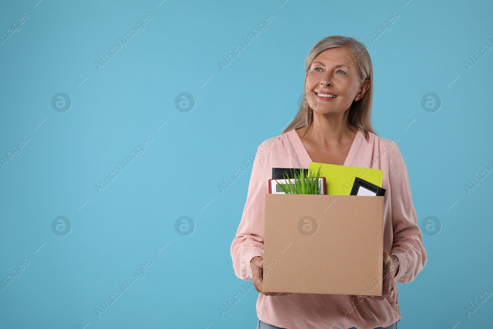 Photo of Happy unemployed senior woman with box of personal office belongings on light blue background. Space for text