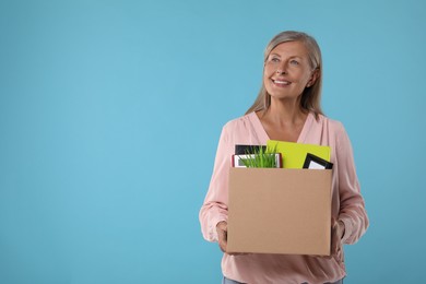 Photo of Happy unemployed senior woman with box of personal office belongings on light blue background. Space for text