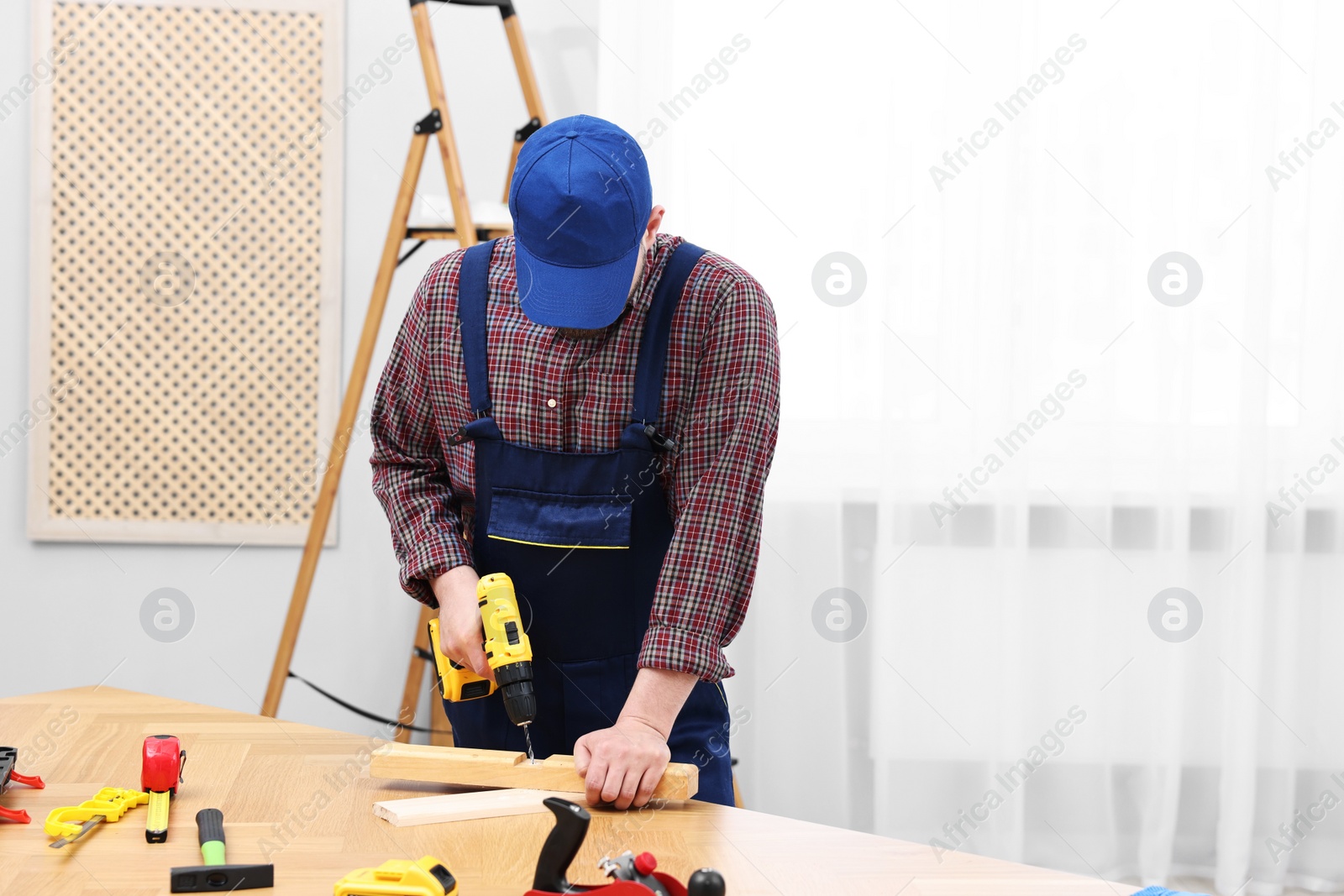 Photo of Young worker using electric drill at table in workshop