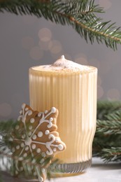 Photo of Tasty eggnog, cookie and fir branches on grey textured table