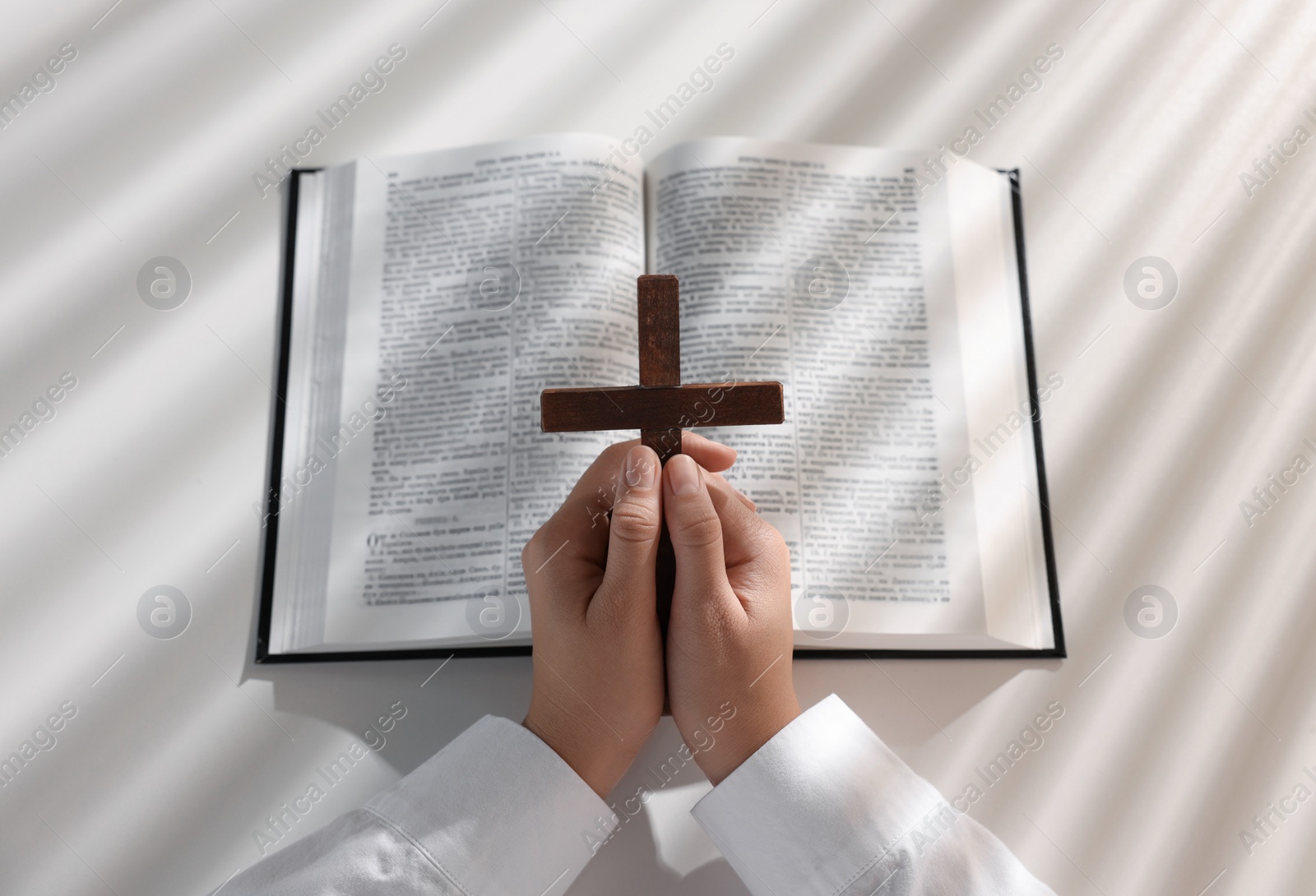 Photo of Above view of woman praying with wooden cross over Bible at white table