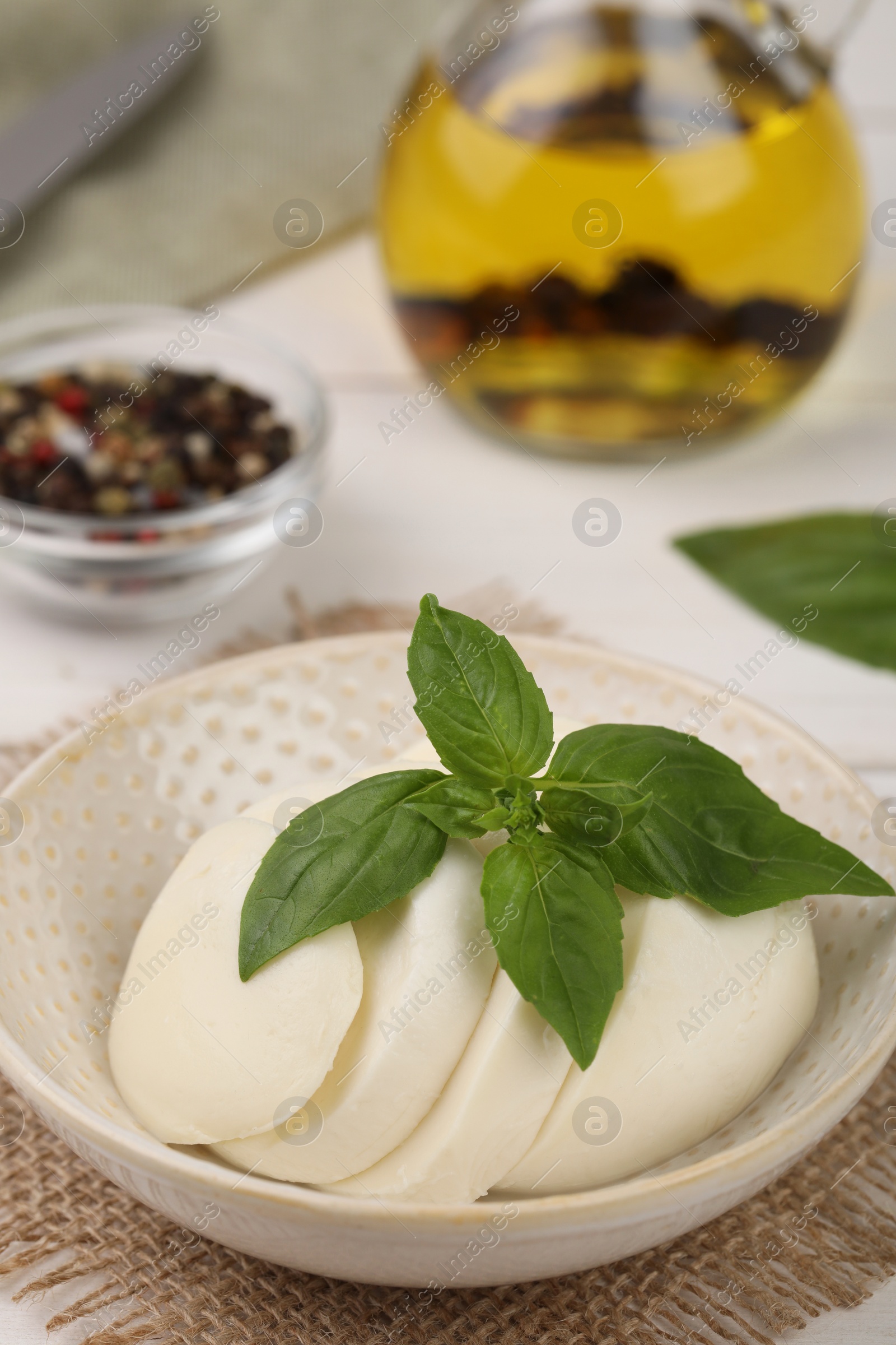 Photo of Tasty mozzarella slices and basil leaves in bowl on table