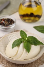 Tasty mozzarella slices and basil leaves in bowl on table