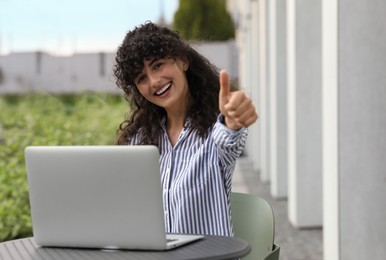 Photo of Happy young woman using modern laptop and showing thumb up outdoors
