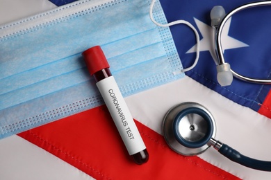 Photo of Test tube with blood sample, medical mask and stethoscope on American flag, flat lay. Coronavirus pandemic in USA