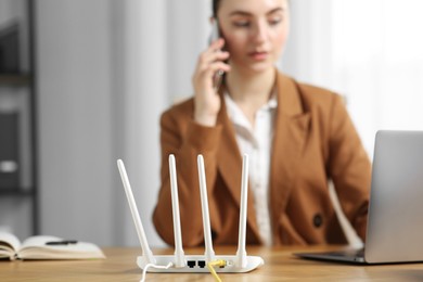 Photo of Woman talking on phone while working with laptop at table indoors, focus on Wi-Fi router