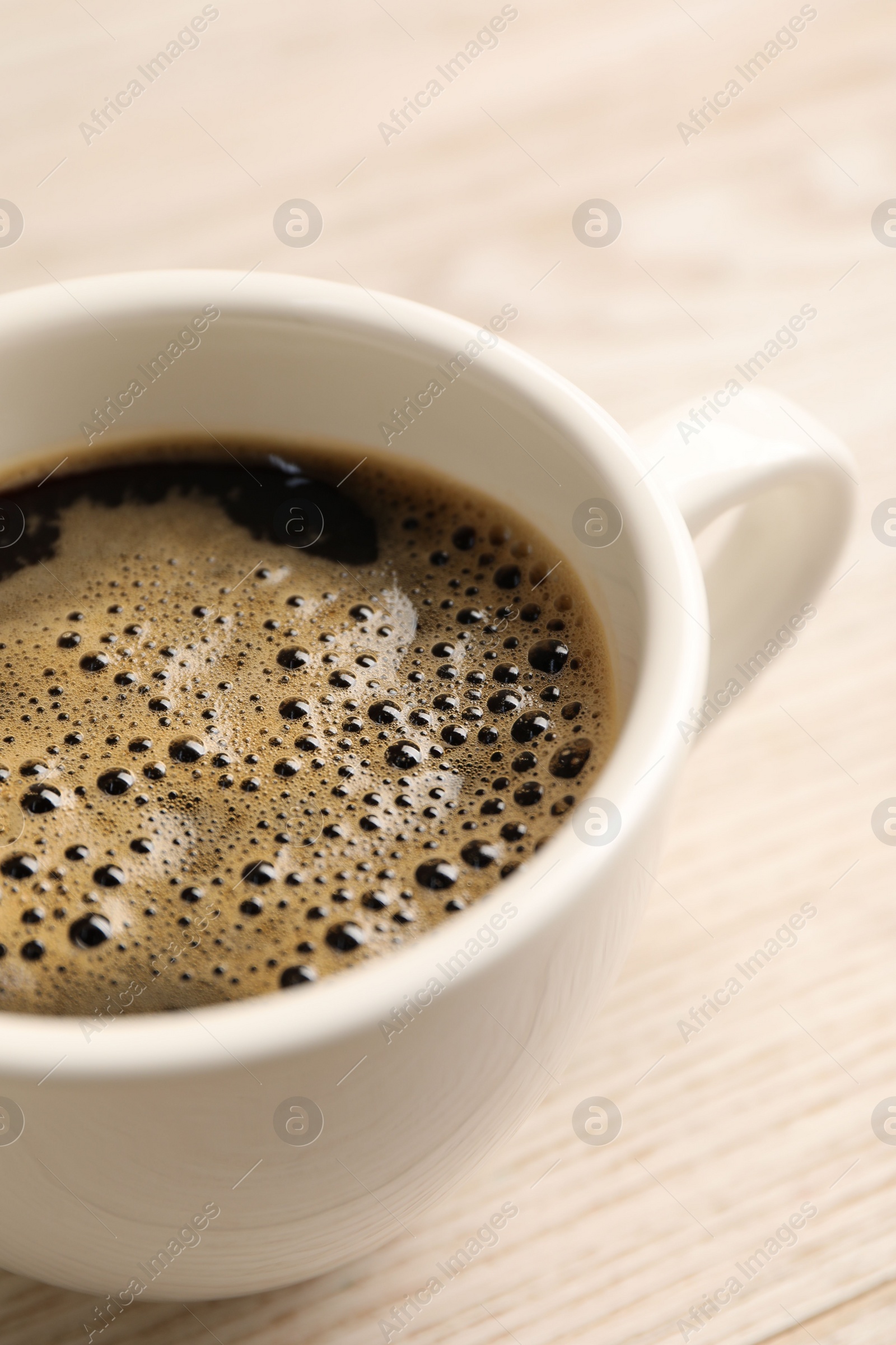 Photo of Aromatic coffee in cup on light wooden table, closeup