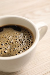 Photo of Aromatic coffee in cup on light wooden table, closeup