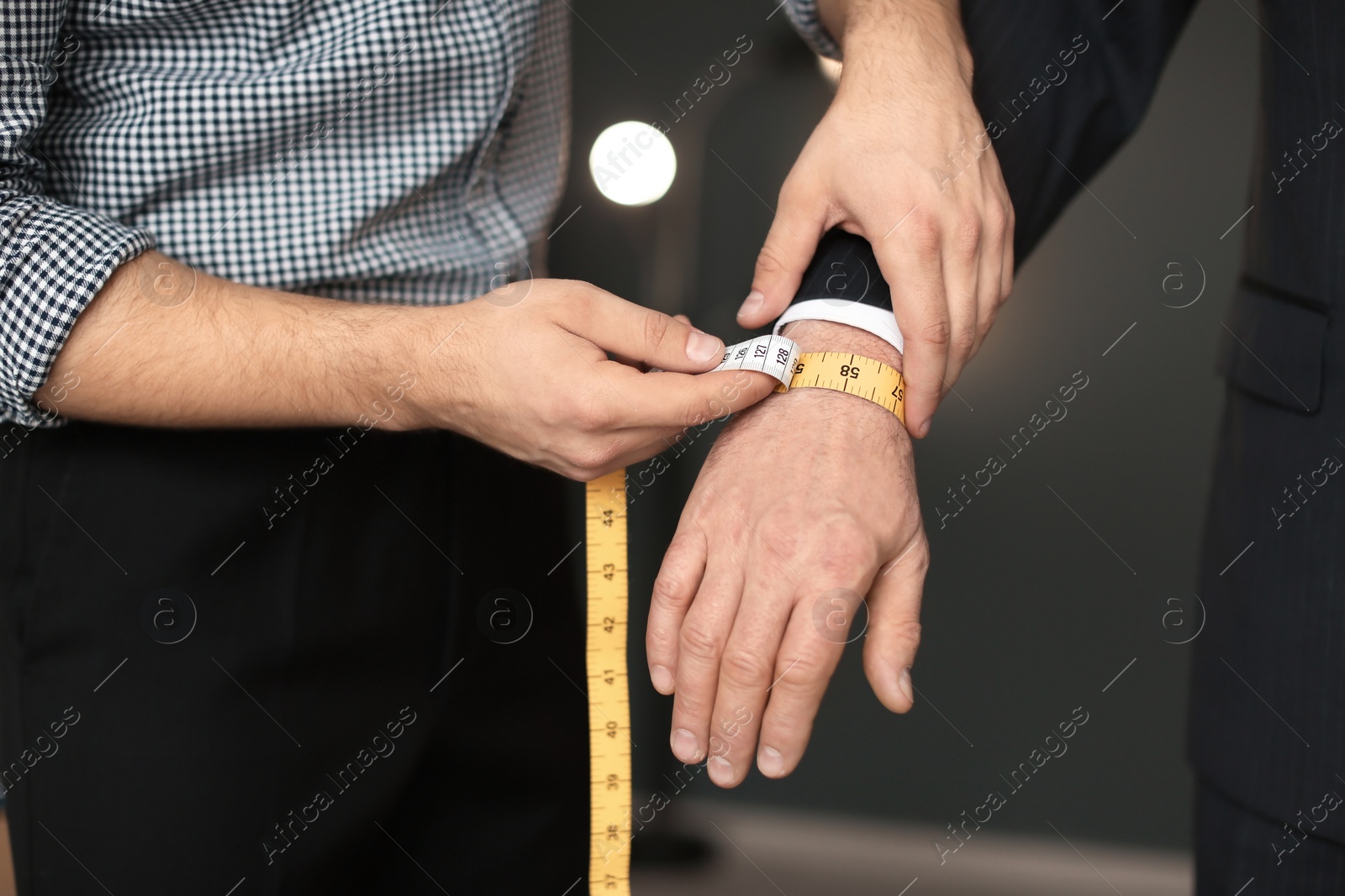 Photo of Young tailor taking client's measurements in atelier, closeup