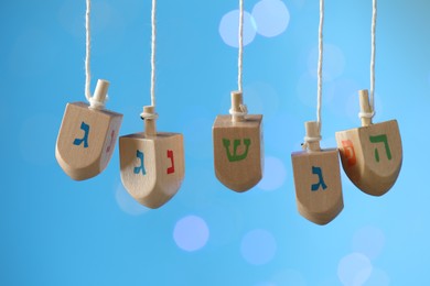 Photo of Hanukkah celebration. Wooden dreidels with jewish letters hanging on twine against light blue background with blurred lights