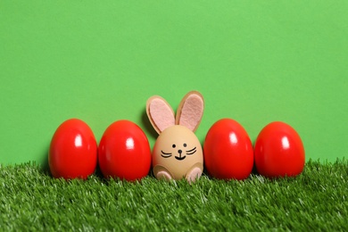 Bright eggs and brown one as Easter bunny on green grass against color background