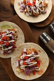 Delicious tacos with vegetables, meat and sauce on wooden table, flat lay