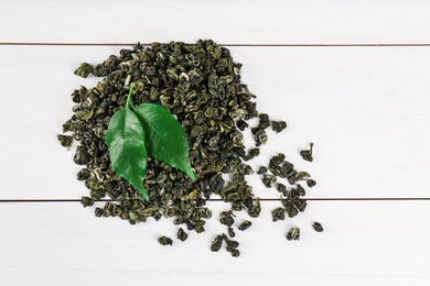 Photo of Heap of dried green tea leaves on white wooden table, top view