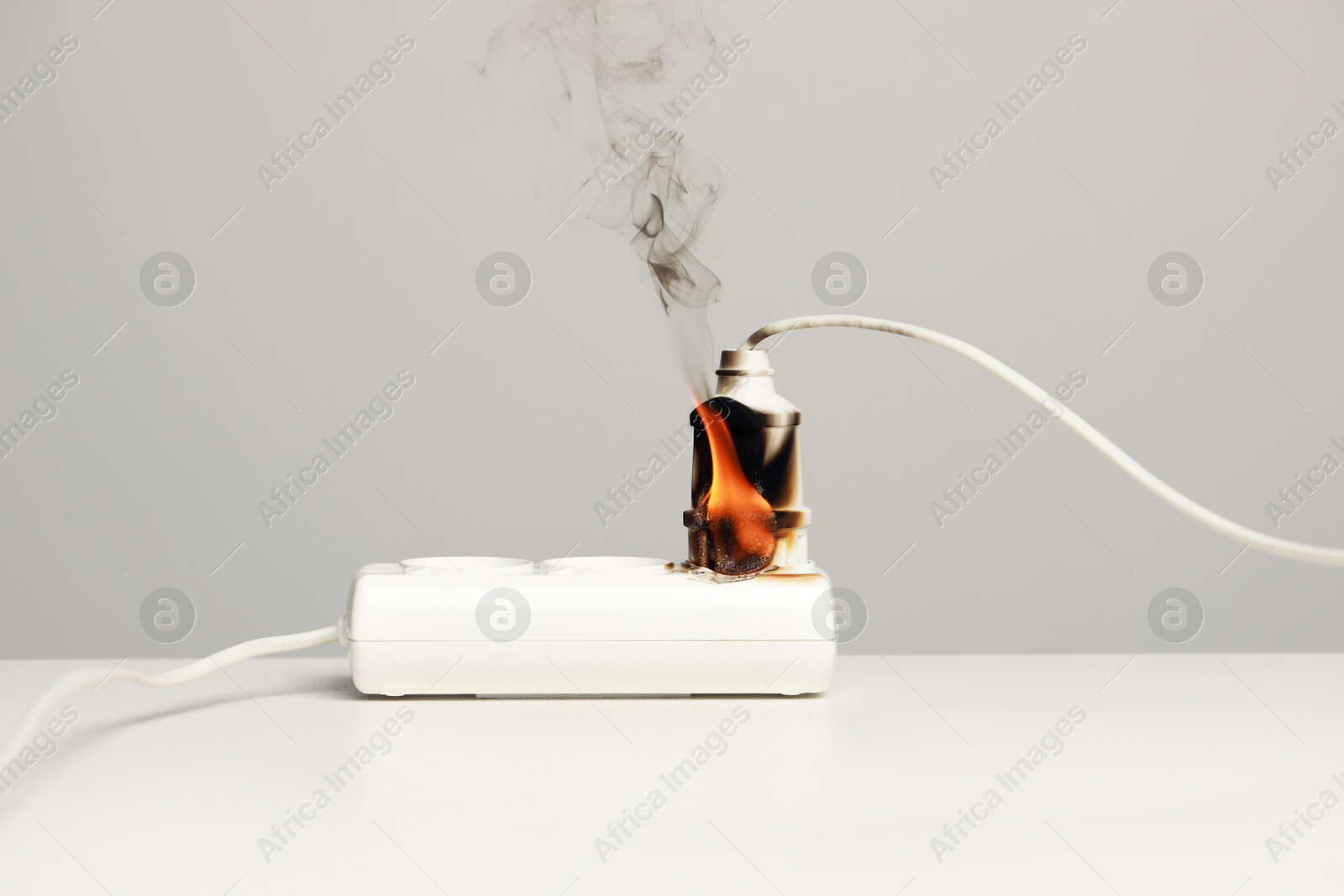 Photo of Inflamed plug in power strip on white table against grey wall. Electrical short circuit