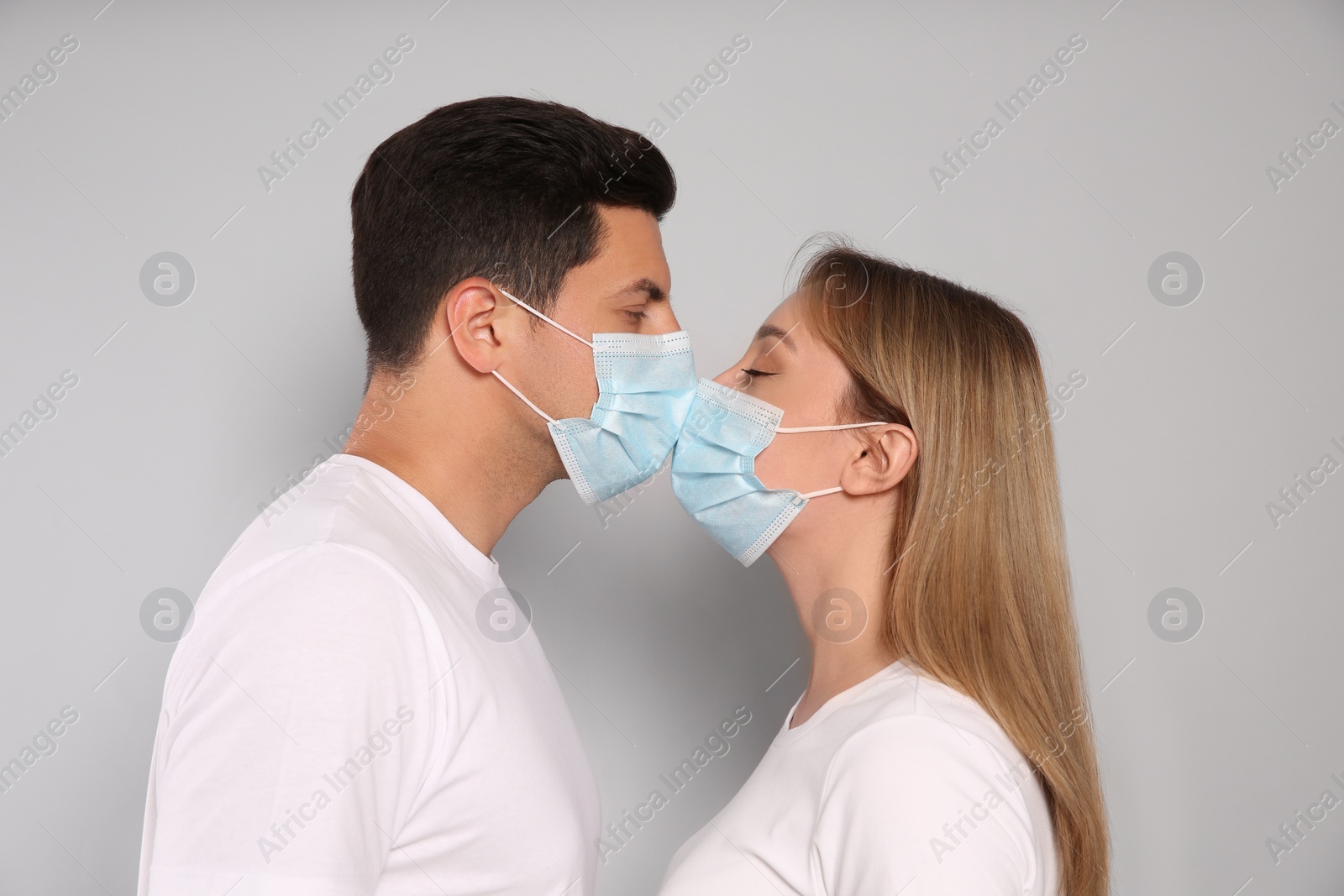 Photo of Couple in medical masks trying to kiss on light background