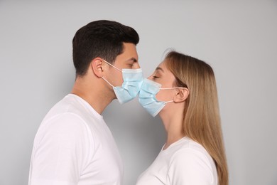 Couple in medical masks trying to kiss on light background