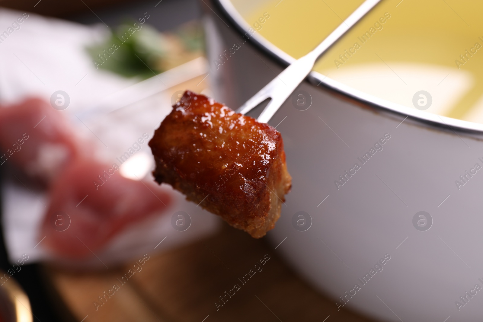 Photo of Fondue pot and fork with fried meat piece on blurred background, closeup