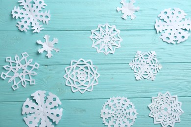 Many paper snowflakes on turquoise wooden background, flat lay
