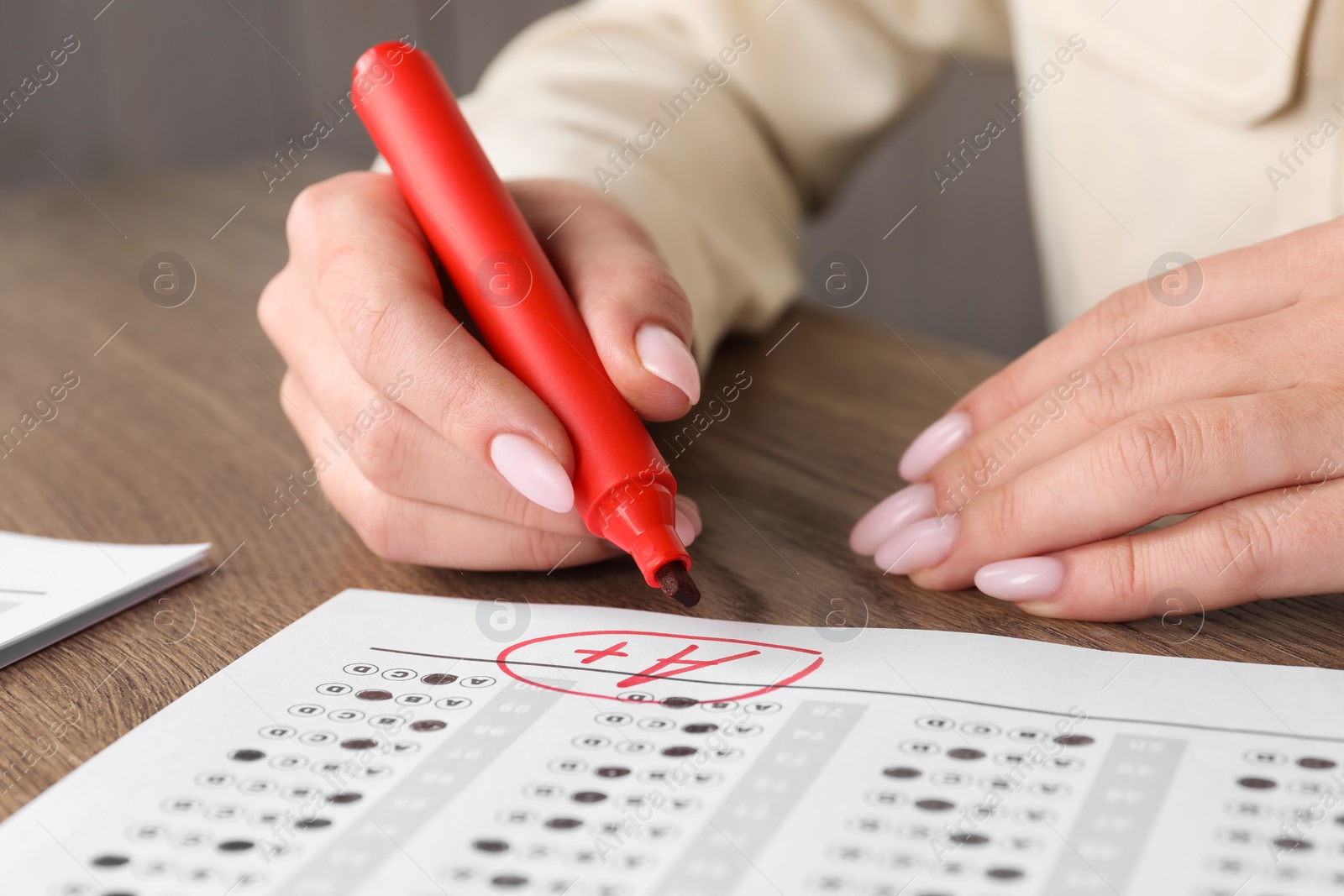 Photo of School grade. Teacher writing letter A with plus symbol on answer sheet at wooden table, closeup