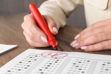 School grade. Teacher writing letter A with plus symbol on answer sheet at wooden table, closeup