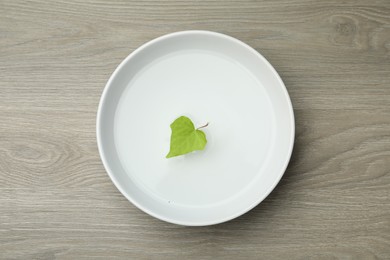 Photo of White bowl with water and green leaf on wooden table, top view