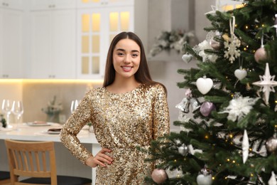 Photo of Portrait of happy woman wearing festive dress near Christmas tree in kitchen