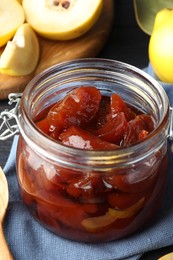 Photo of Quince jam in glass jar and fresh raw fruits on table, closeup