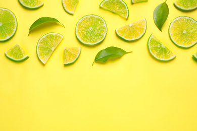 Photo of Juicy fresh lime slices and green leaves on yellow background, flat lay. Space for text