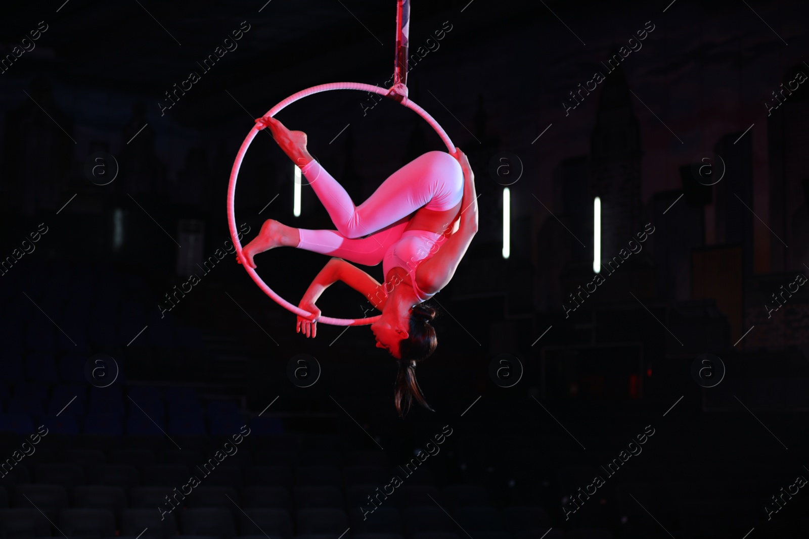 Photo of Young woman performing acrobatic element on aerial ring against dark background