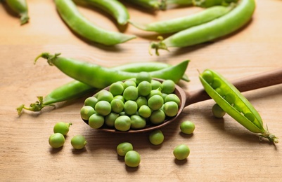 Photo of Spoon with green peas on wooden table, closeup