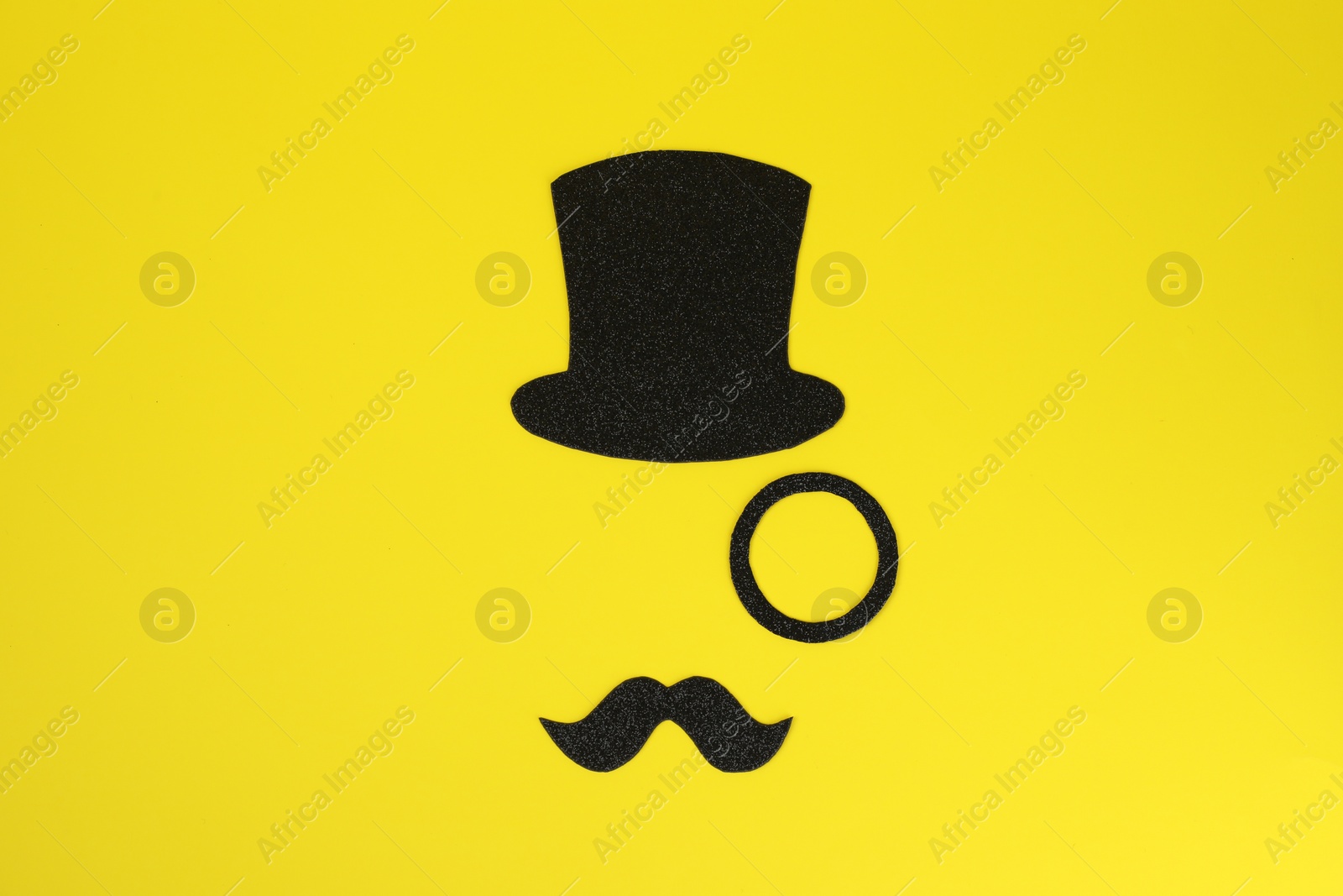 Photo of Man's face made of fake mustache, hat and monocle on yellow background, top view