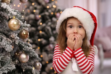 Photo of Surprised child near Christmas tree at home. Space for text