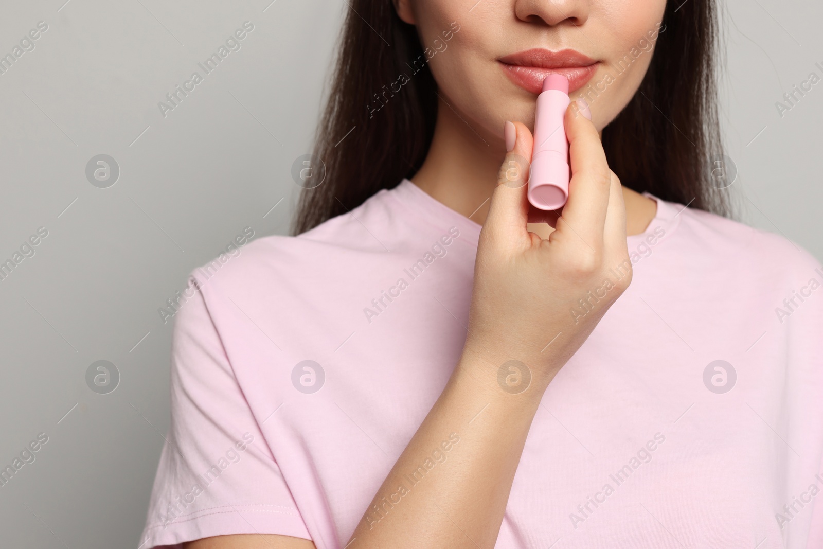 Photo of Young woman applying lip balm on grey background, closeup