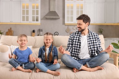 Father with children meditating together on sofa at home. Harmony and zen