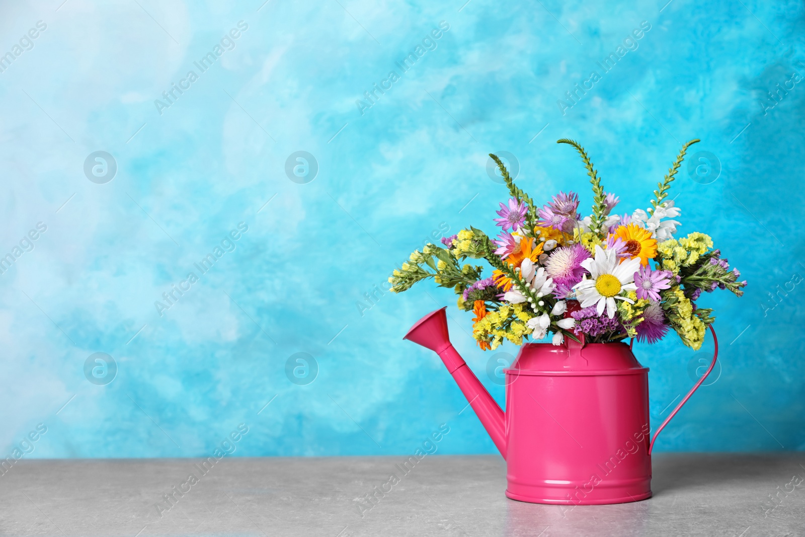 Photo of Watering can with beautiful wild flowers on table against color background