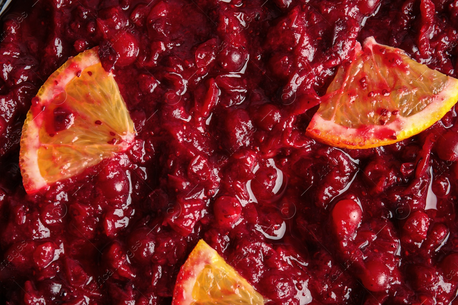 Photo of Tasty cranberry sauce with citrus fruit slices as background, top view
