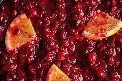 Tasty cranberry sauce with citrus fruit slices as background, top view