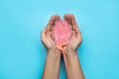 Photo of Woman holding paper cutout of small intestine on turquoise background, top view